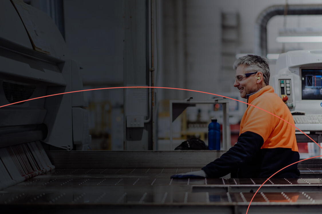 A factory worker wearing safety glasses stands next to a control panel.