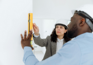 Two construction workers in hard hats use a level on a wall. 